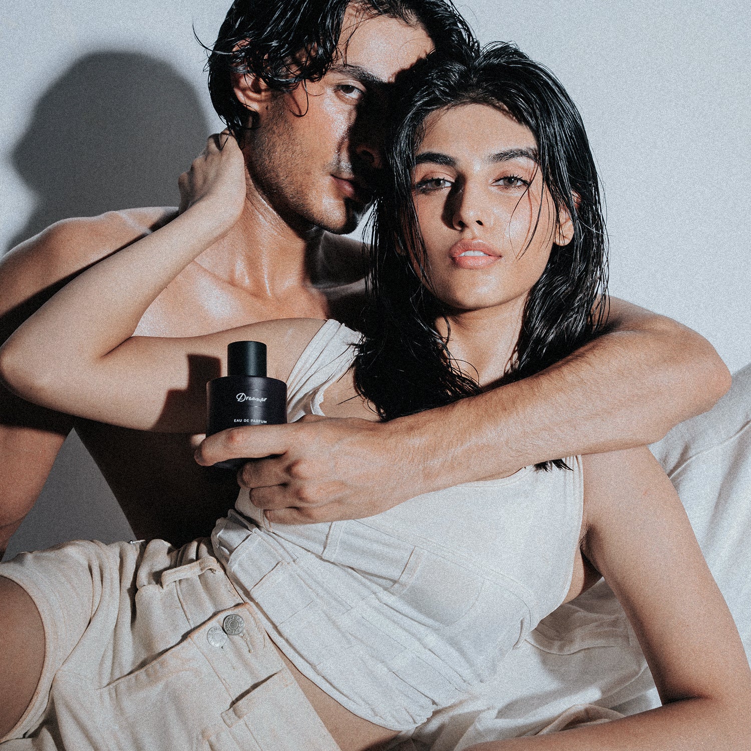 men and women laying with dreamer unisex perfume in hand